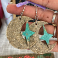 Earrings with star and crescent moon design held by a hand.